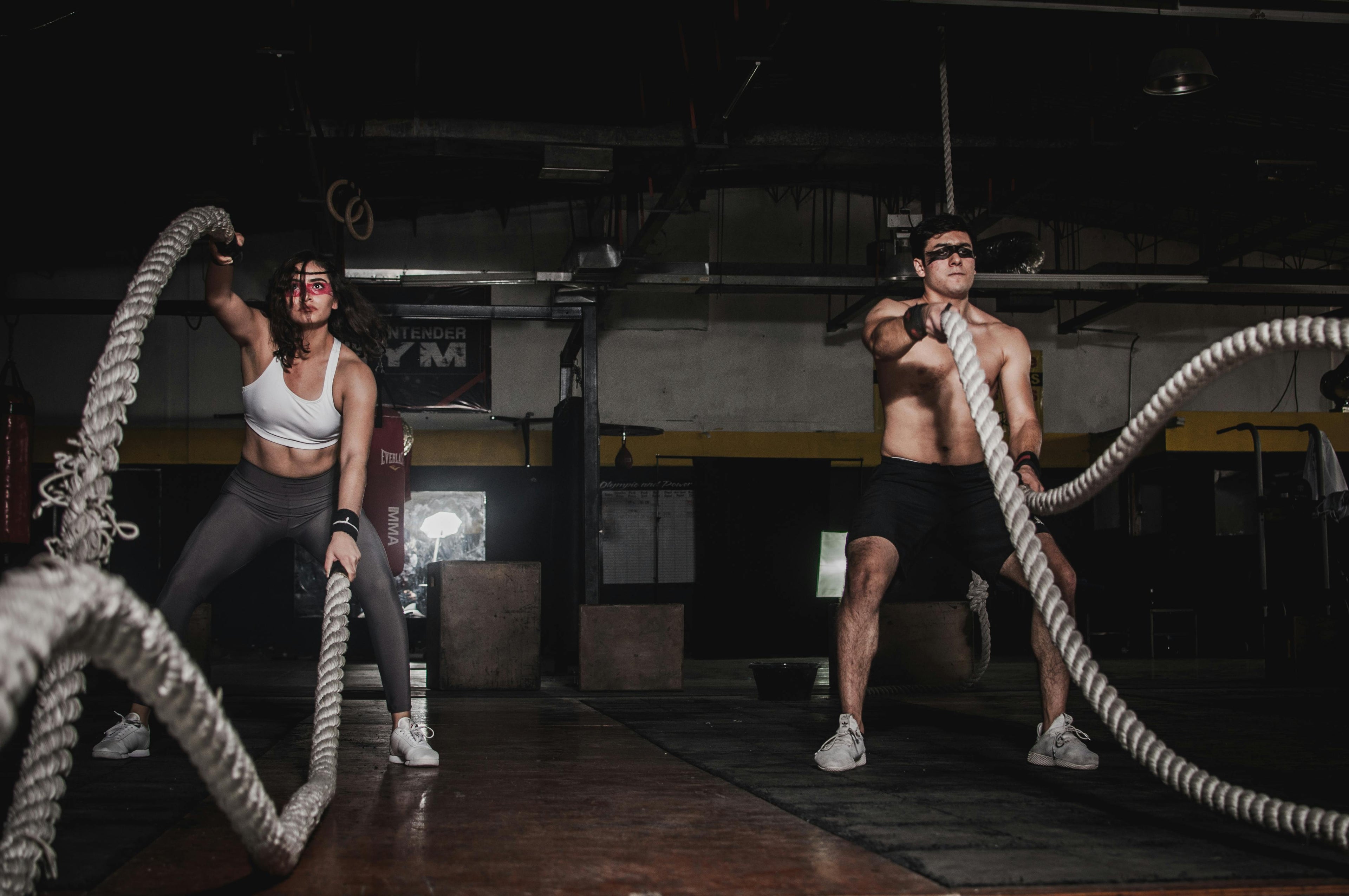Two people doing battle rope exercises in a gym