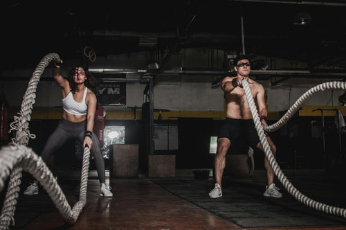 Two people doing battle rope exercises in a gym