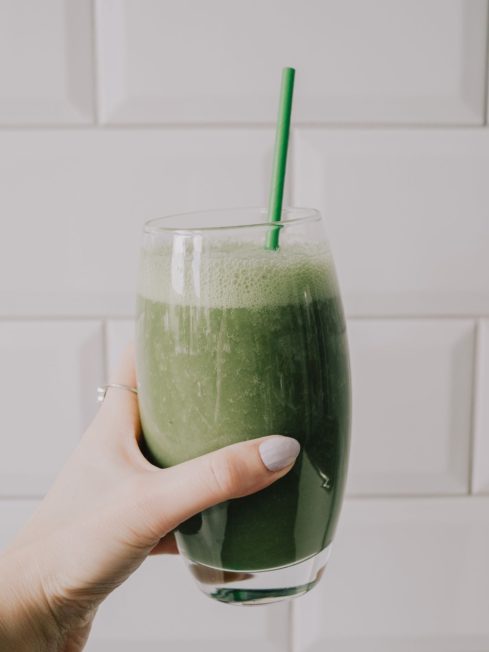 Hand holding a vibrant green smoothie with a straw