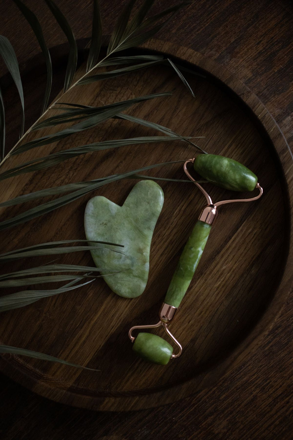 Gua sha and jade roller on a wooden surface