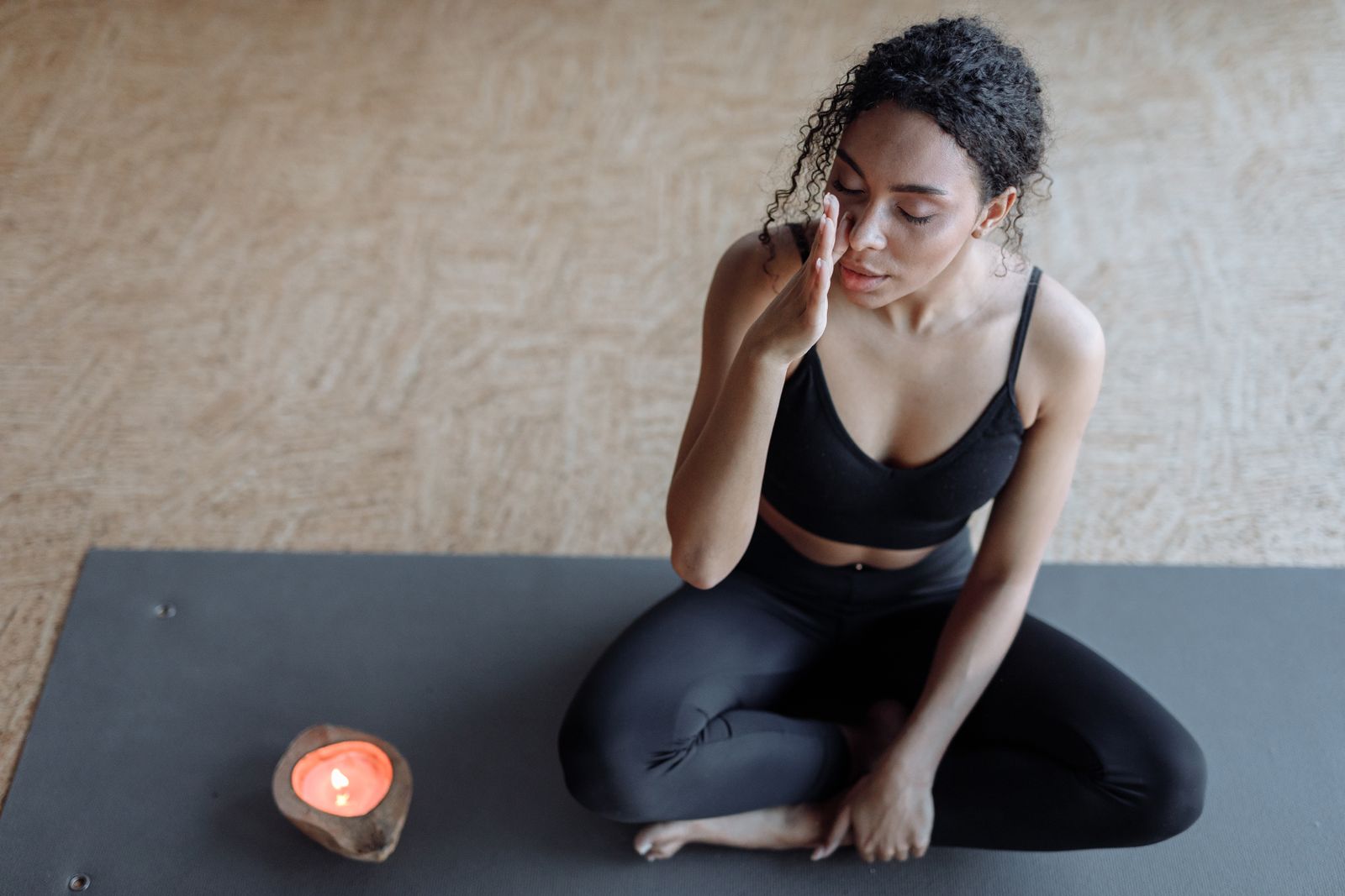 Woman meditating on a yoga mat beside a lit candle