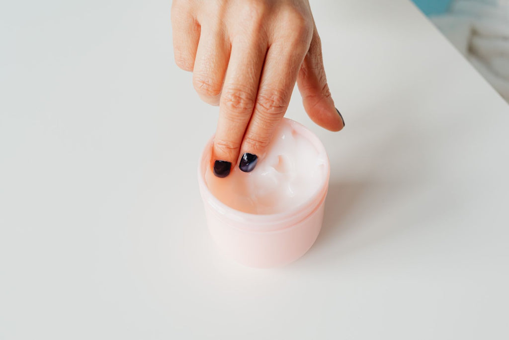 Fingertip dipping into a jar of cream